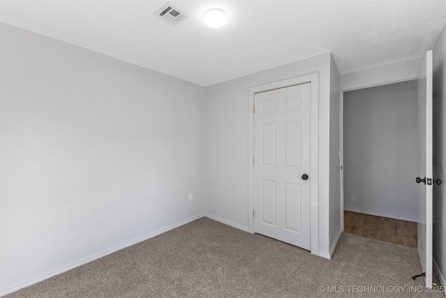 unfurnished bedroom featuring carpet, visible vents, a textured ceiling, and baseboards