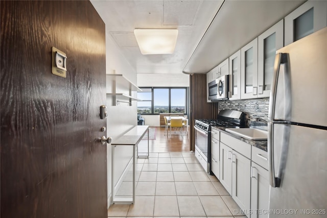 kitchen with light tile patterned floors, decorative backsplash, stainless steel appliances, white cabinetry, and a sink