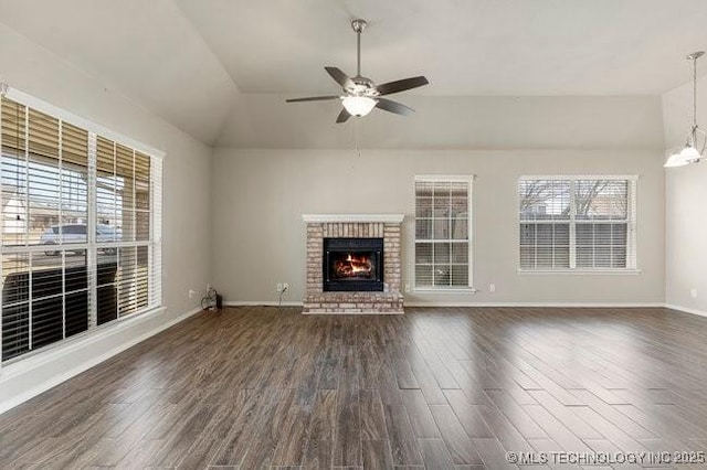 unfurnished living room featuring a brick fireplace, dark wood finished floors, a wealth of natural light, and ceiling fan with notable chandelier