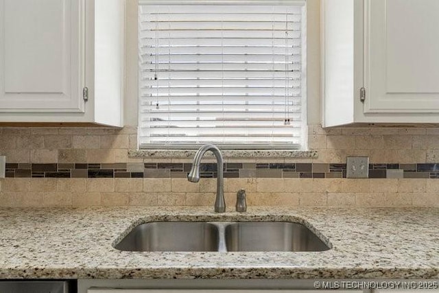 kitchen with decorative backsplash, a sink, light stone countertops, and white cabinets