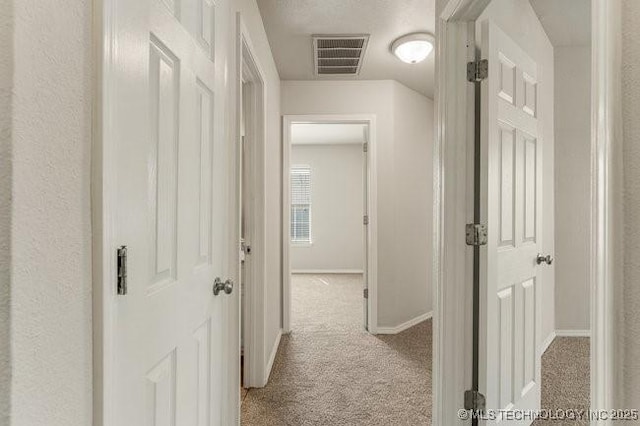 hallway with light carpet, visible vents, and baseboards