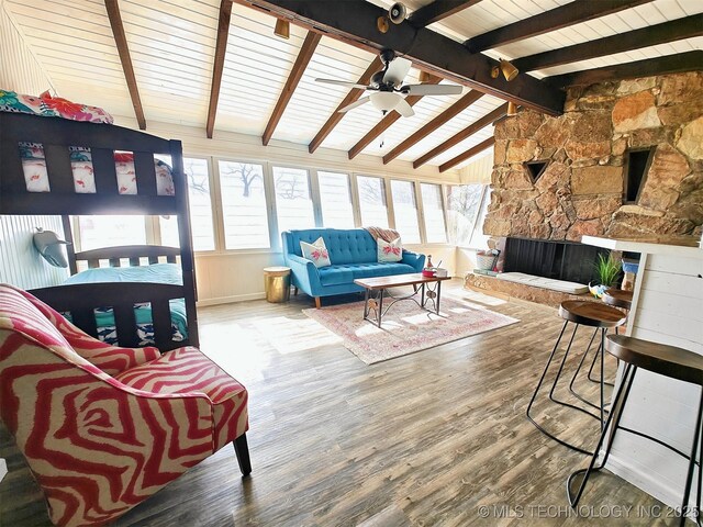 interior space featuring a ceiling fan, a stone fireplace, lofted ceiling with beams, and wood finished floors