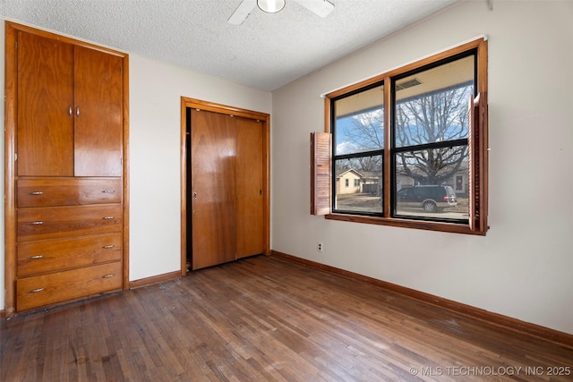 unfurnished bedroom featuring baseboards, a ceiling fan, dark wood-style floors, a textured ceiling, and a closet