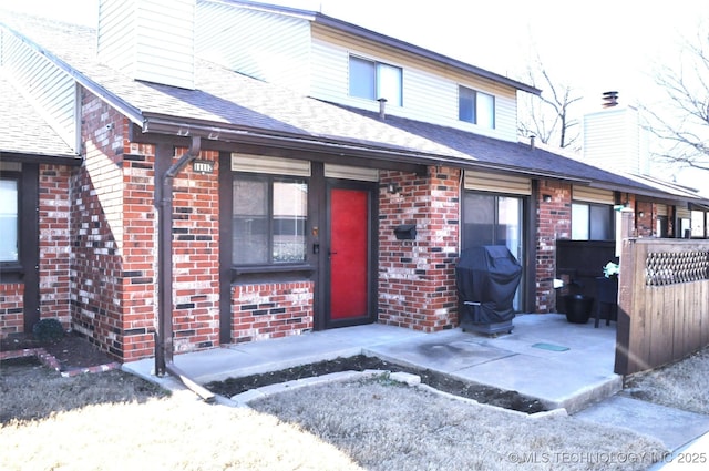 view of front of home with brick siding, a chimney, and a shingled roof