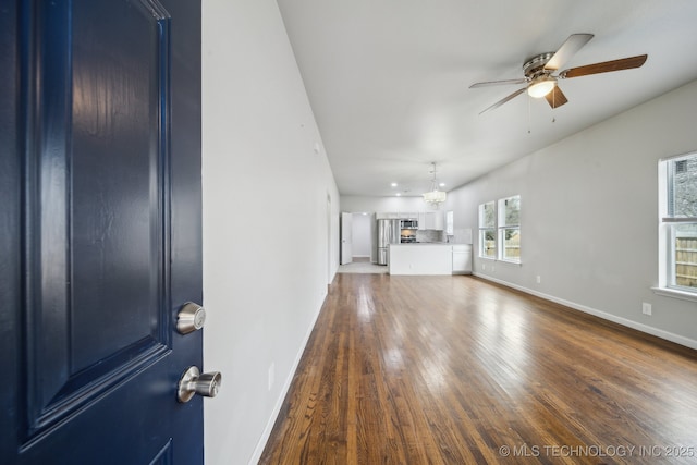 unfurnished living room featuring baseboards, wood finished floors, and ceiling fan with notable chandelier