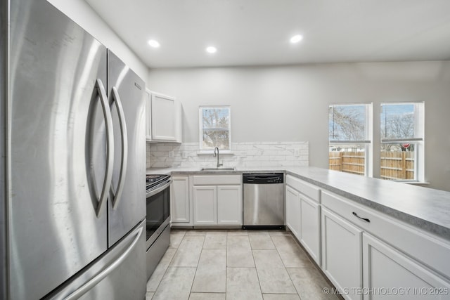 kitchen with stainless steel appliances, light countertops, backsplash, white cabinetry, and a sink