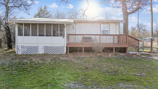 rear view of property featuring metal roof, a yard, a deck, and a sunroom