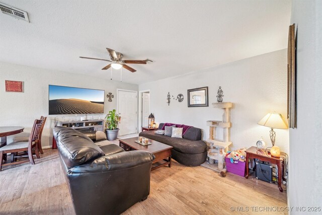 living area with visible vents, ceiling fan, a fireplace, and wood finished floors