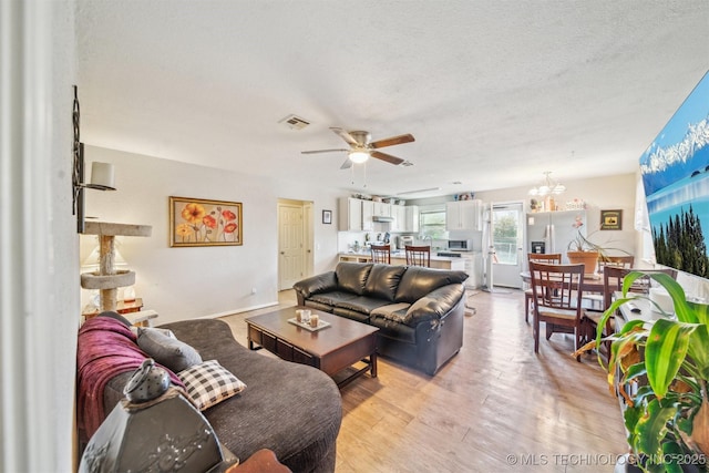 living area featuring light wood-style floors, visible vents, a textured ceiling, and ceiling fan with notable chandelier