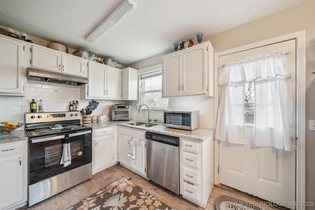 kitchen featuring stainless steel appliances, light wood-type flooring, under cabinet range hood, white cabinetry, and a sink