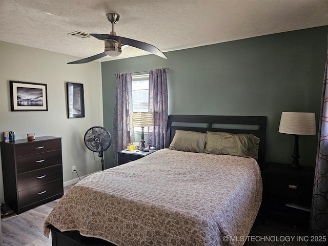 bedroom featuring baseboards, visible vents, a ceiling fan, wood finished floors, and a textured ceiling
