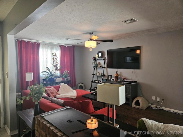 living room with baseboards, visible vents, a ceiling fan, wood finished floors, and a textured ceiling