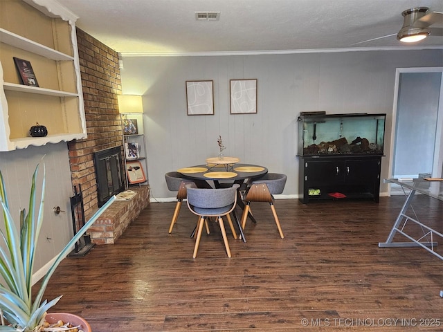 dining room with crown molding, visible vents, dark wood-type flooring, a brick fireplace, and baseboards