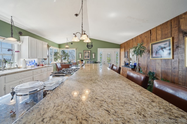 3126 E 490th Rd, Pryor, OK 74361 - kitchen featuring decorative light fixtures, light stone countertops, a sink, white cabinets, and wooden walls