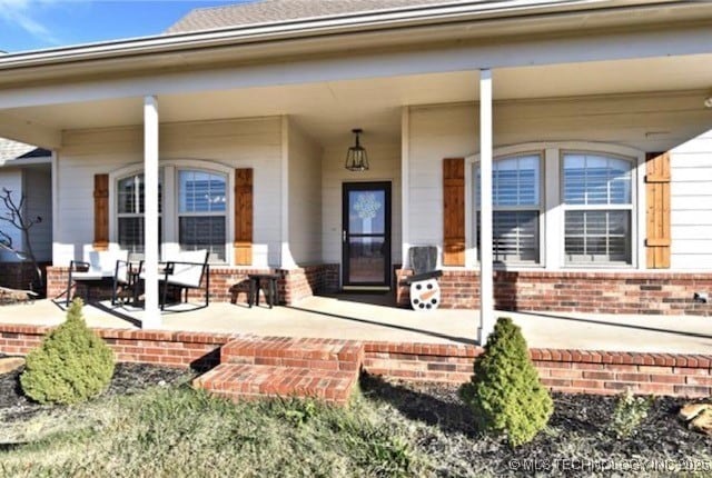 doorway to property featuring a porch and brick siding