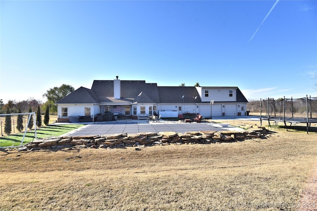 rear view of house featuring a trampoline, a chimney, a lawn, a patio area, and fence