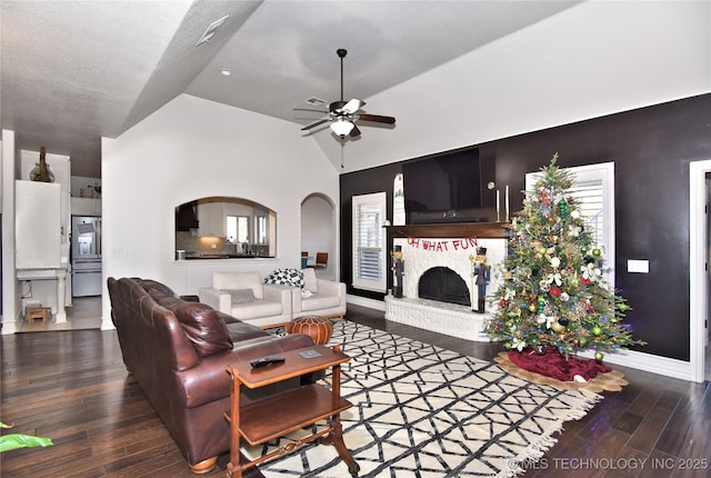 living room with ceiling fan, a stone fireplace, wood finished floors, high vaulted ceiling, and baseboards