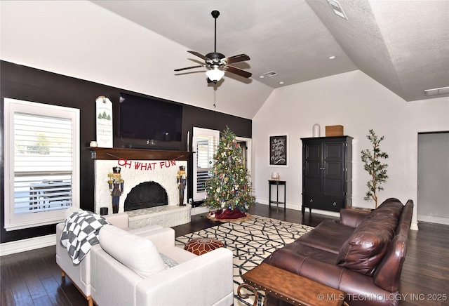 living area featuring baseboards, a fireplace with raised hearth, ceiling fan, wood finished floors, and vaulted ceiling