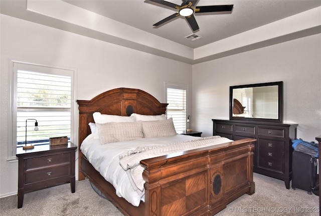 bedroom featuring a ceiling fan, a raised ceiling, visible vents, and light carpet