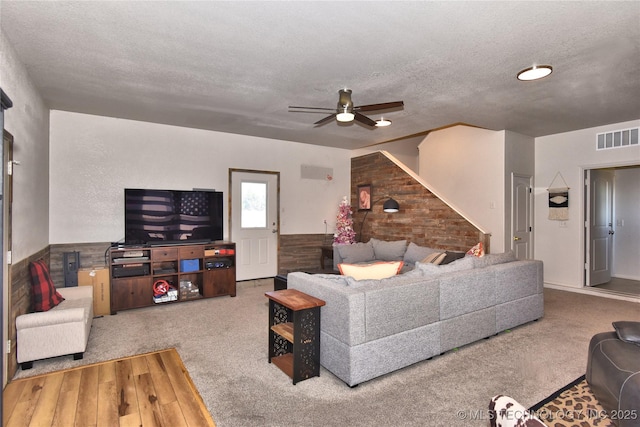 carpeted living area featuring a textured ceiling, ceiling fan, a wainscoted wall, and visible vents