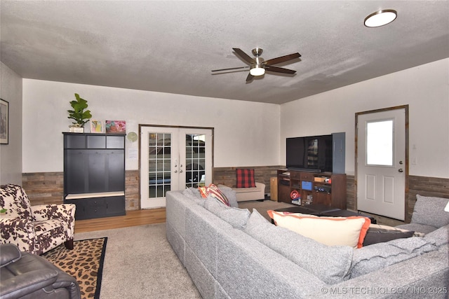 living room with french doors, wainscoting, ceiling fan, and a textured ceiling