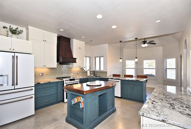 kitchen with blue cabinets, a peninsula, a sink, high end appliances, and custom range hood