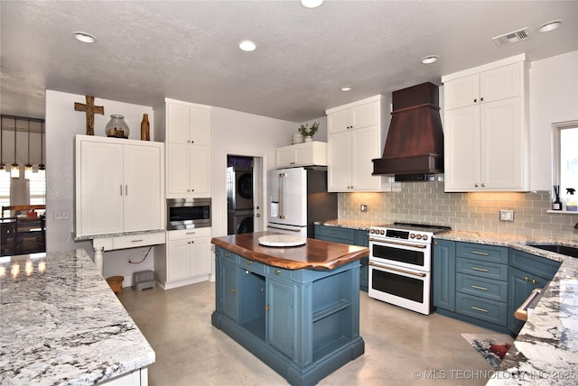 kitchen featuring stacked washer and dryer, visible vents, premium appliances, custom exhaust hood, and blue cabinetry