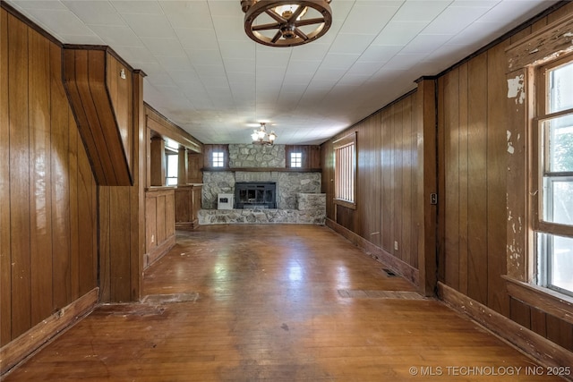 unfurnished living room featuring wood walls, wood finished floors, and a stone fireplace