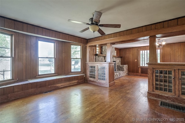 unfurnished living room with wood walls, wood-type flooring, visible vents, and ceiling fan with notable chandelier