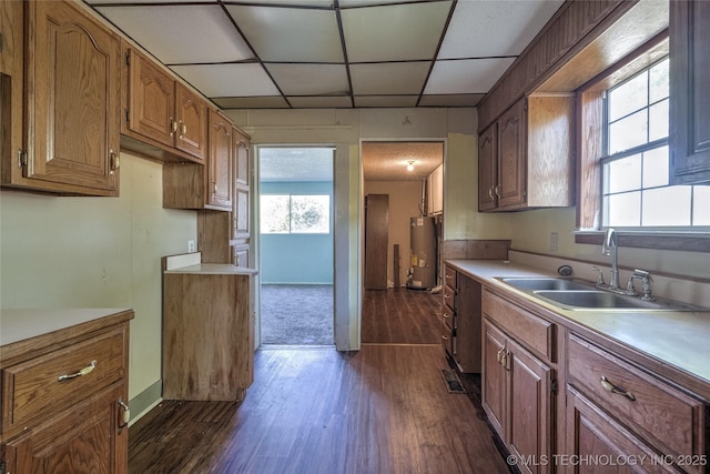 kitchen featuring gas water heater, light countertops, a sink, and a drop ceiling