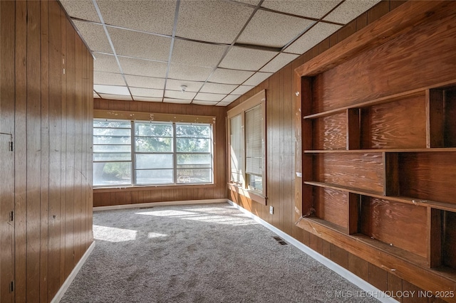 spare room with baseboards, visible vents, carpet flooring, a paneled ceiling, and wood walls