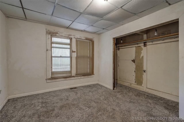 unfurnished bedroom featuring carpet floors, a closet, a paneled ceiling, and baseboards