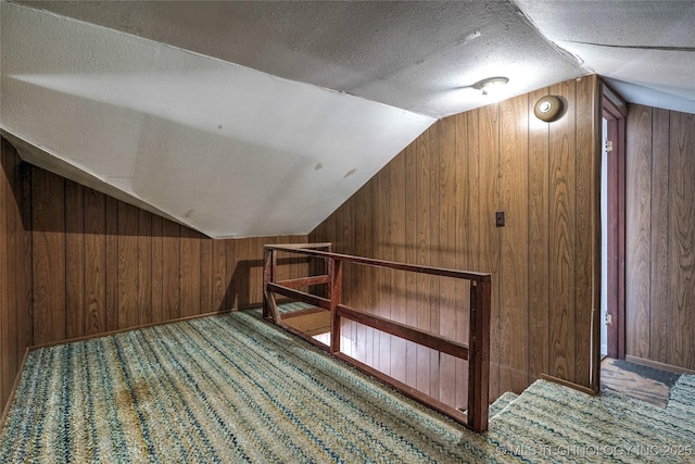 additional living space featuring carpet, vaulted ceiling, wood walls, a textured ceiling, and baseboards