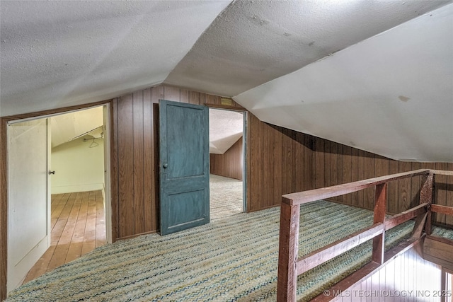 additional living space featuring lofted ceiling, wooden walls, a textured ceiling, and wood finished floors