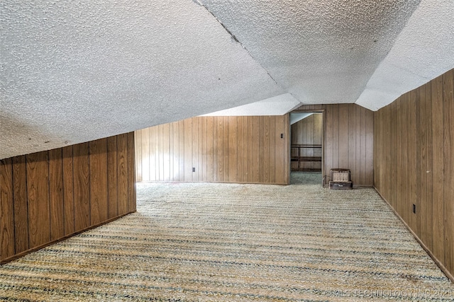 additional living space with vaulted ceiling, wooden walls, and a textured ceiling