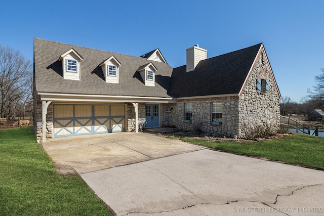 cape cod-style house featuring a chimney, a front yard, a garage, stone siding, and driveway