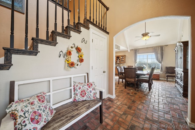 interior space with brick floor, arched walkways, lofted ceiling, a ceiling fan, and baseboards