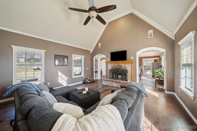 living area with arched walkways, dark wood-style flooring, a fireplace, crown molding, and baseboards