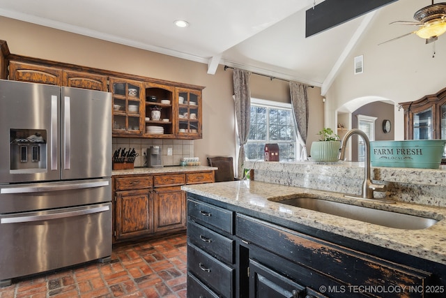 kitchen with stainless steel fridge, decorative backsplash, ornamental molding, brick floor, and a sink