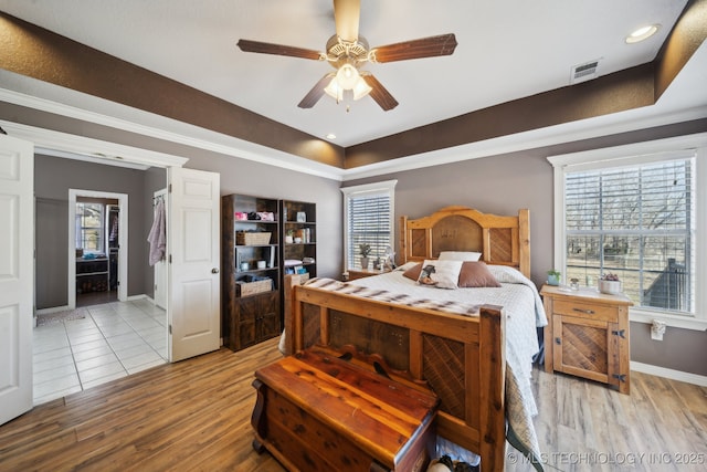 bedroom featuring ceiling fan, wood finished floors, visible vents, baseboards, and a raised ceiling