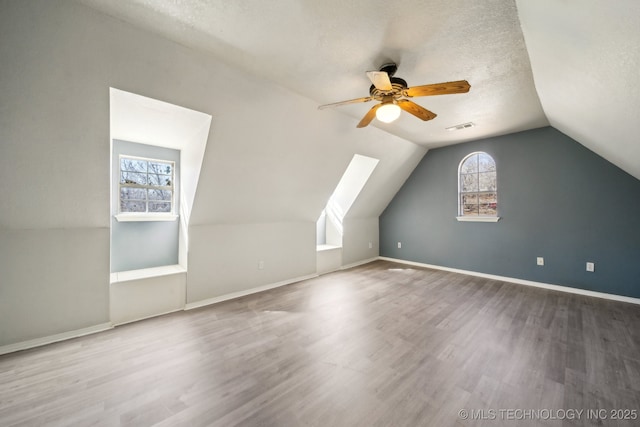 bonus room featuring a textured ceiling, vaulted ceiling, wood finished floors, and visible vents