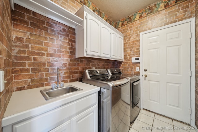 clothes washing area featuring cabinet space, light tile patterned floors, brick wall, separate washer and dryer, and a sink