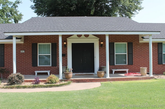 view of front facade featuring covered porch, a shingled roof, a front yard, and brick siding