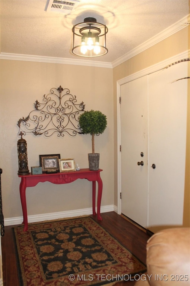 entryway with visible vents, crown molding, baseboards, and wood finished floors