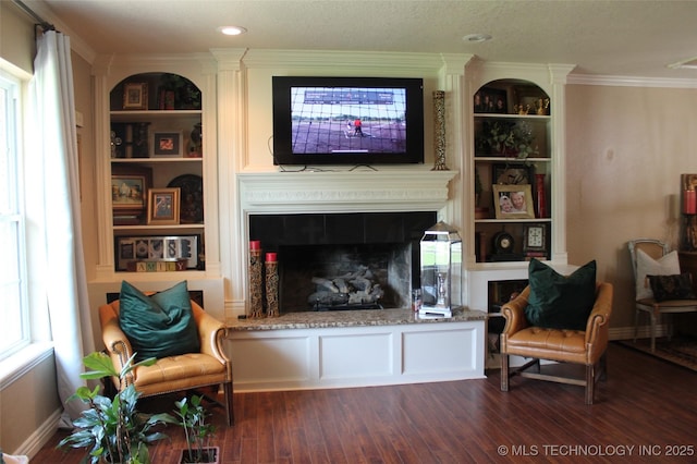 sitting room with built in shelves, ornamental molding, dark wood-style flooring, and a tile fireplace