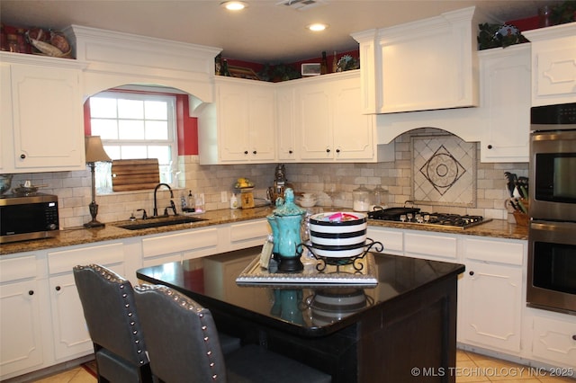 kitchen featuring a sink, white cabinetry, appliances with stainless steel finishes, decorative backsplash, and dark stone countertops