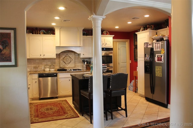 kitchen with arched walkways, stainless steel appliances, decorative backsplash, white cabinetry, and light tile patterned flooring