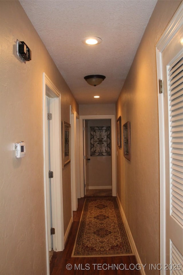 corridor featuring a textured ceiling, baseboards, dark wood-type flooring, and a textured wall