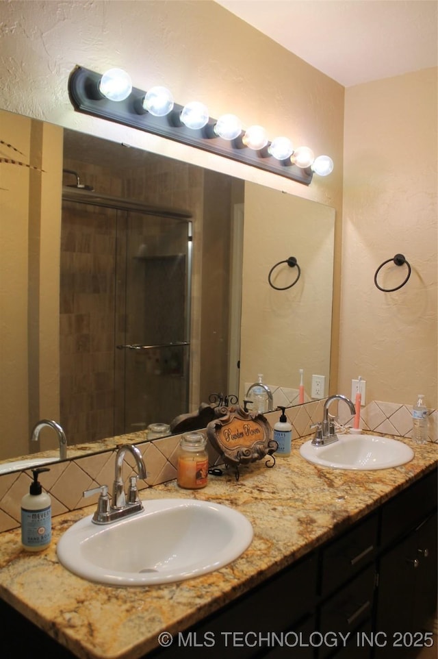 full bathroom featuring double vanity, backsplash, a sink, and a shower stall