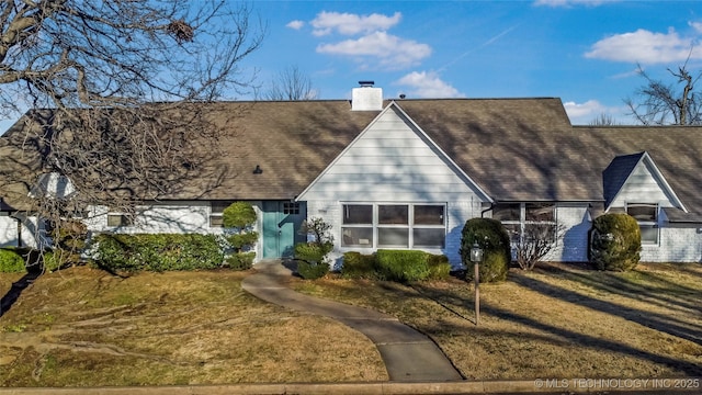 view of front of property with roof with shingles, a front lawn, and a chimney